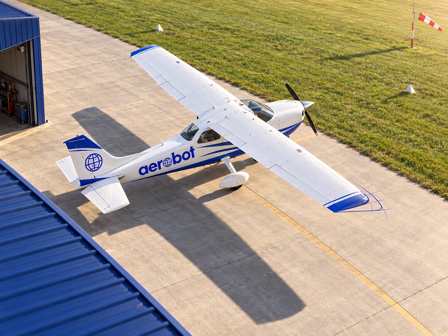 Illustration Aerobot : vue plongeante sur un avion léger au seuil du hangar, avec un discret tracé bleu sur l’aile.